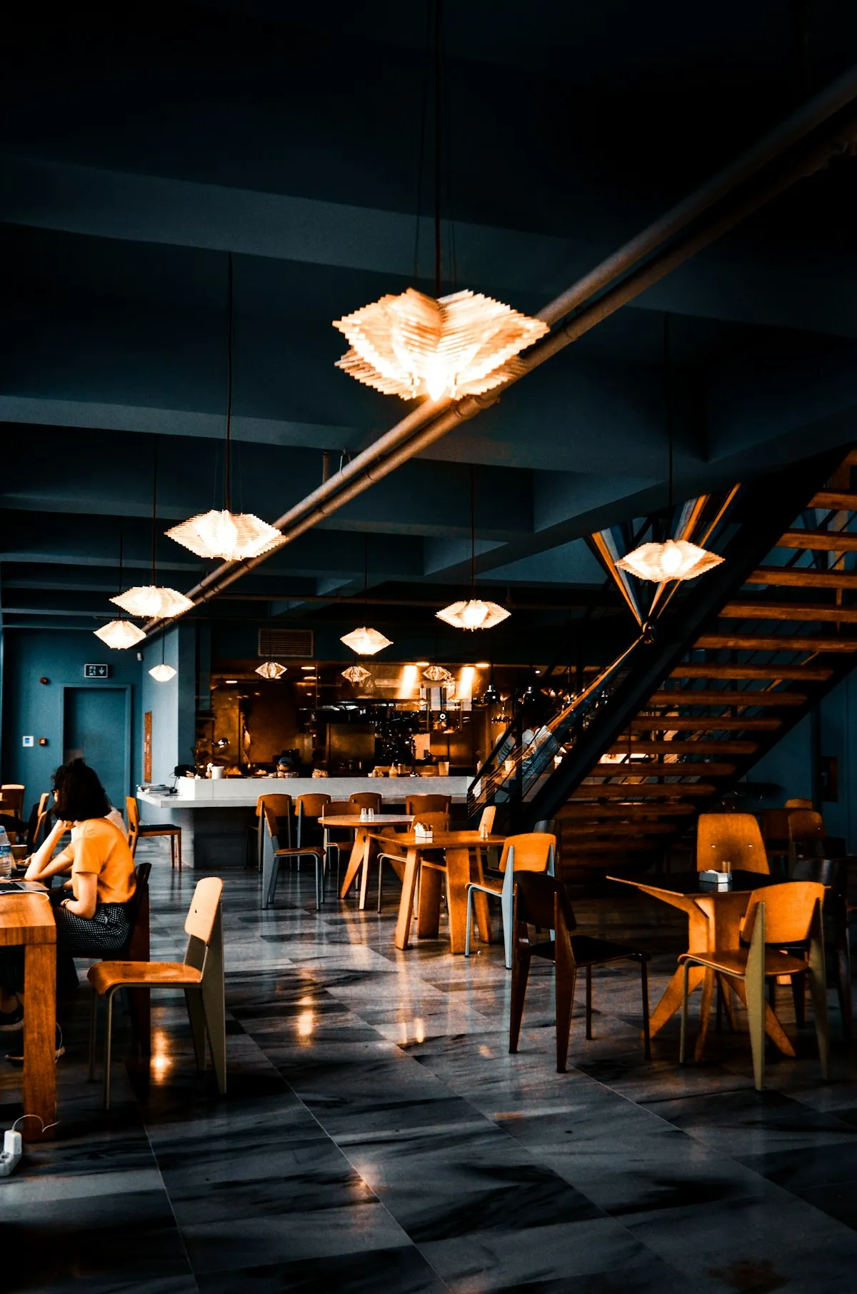 Sala del restaurante en penumbra, con lámparas colgantes encendidas y una escalera al fondo